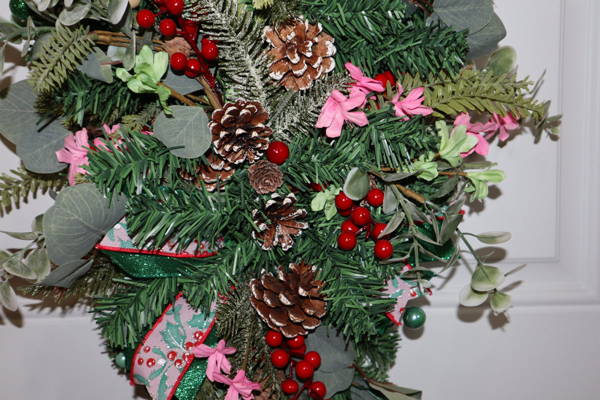 Pinecones red berries pink flowers and greenery on Christmas teardrop swag