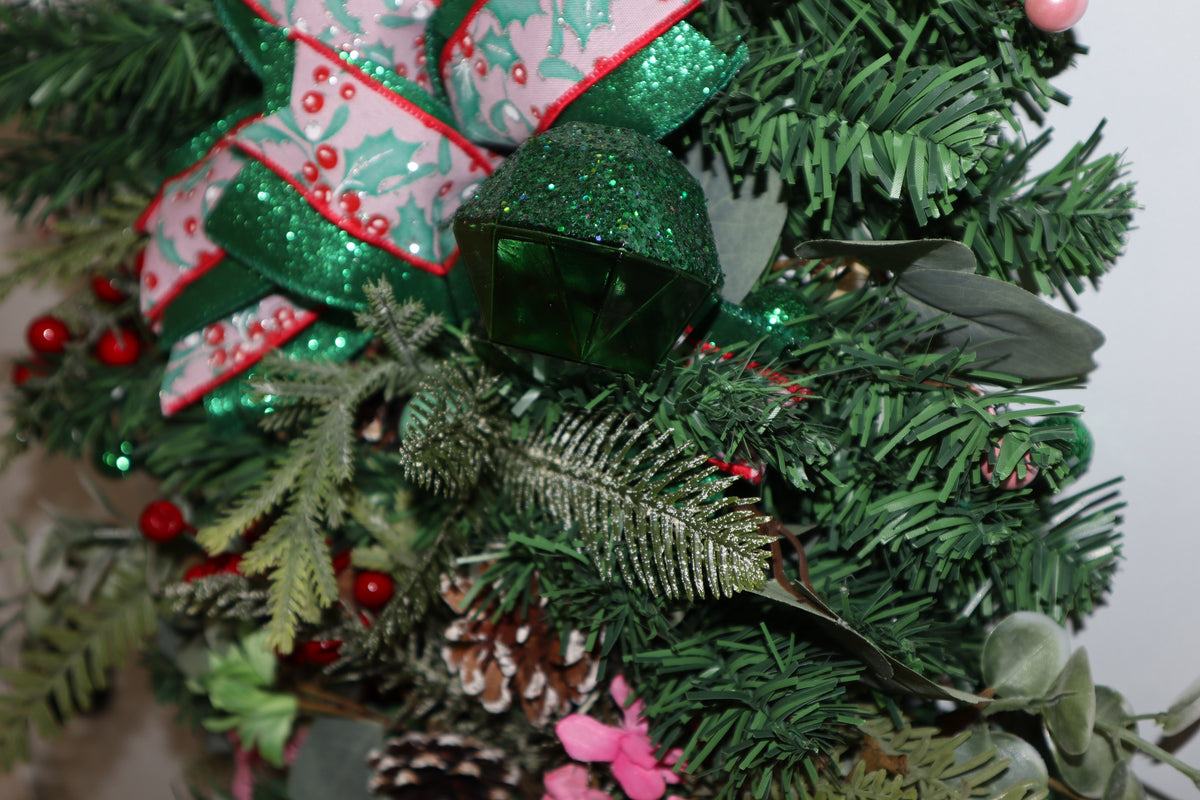 Faceted emerald green gem nestled in Christmas greenery and ribbon