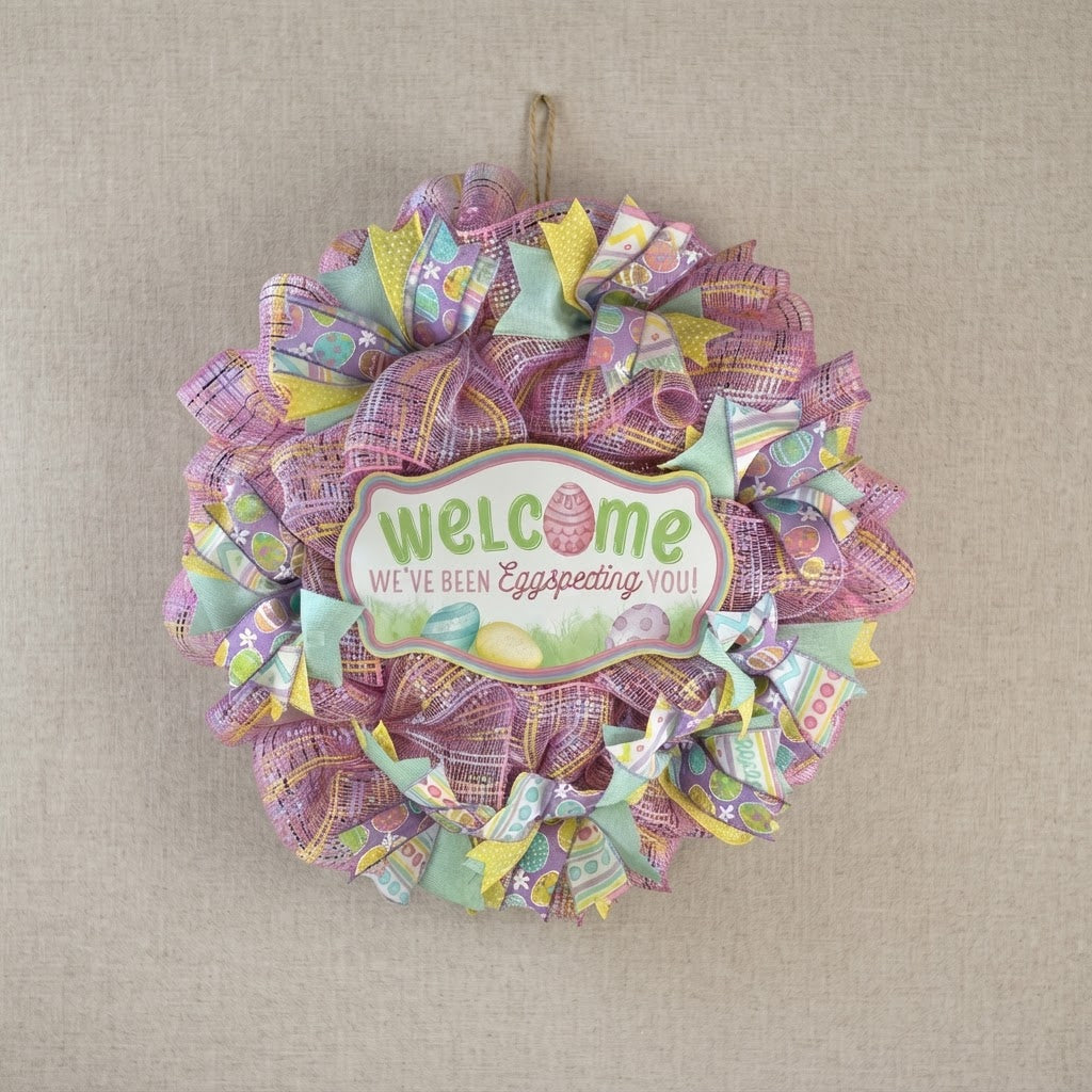 Handmade pastel Easter wreath with wooden welcome sign hanging on a neutral fabric background