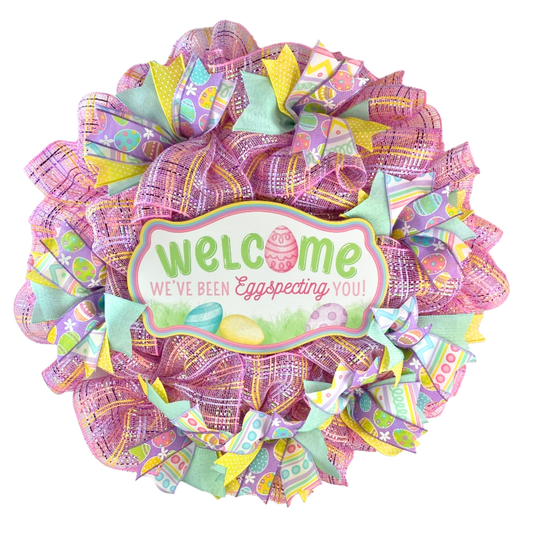 Welcome Easter pastel mesh wreath with wooden welcome sign, pink mesh, and colorful spring ribbons on a white background