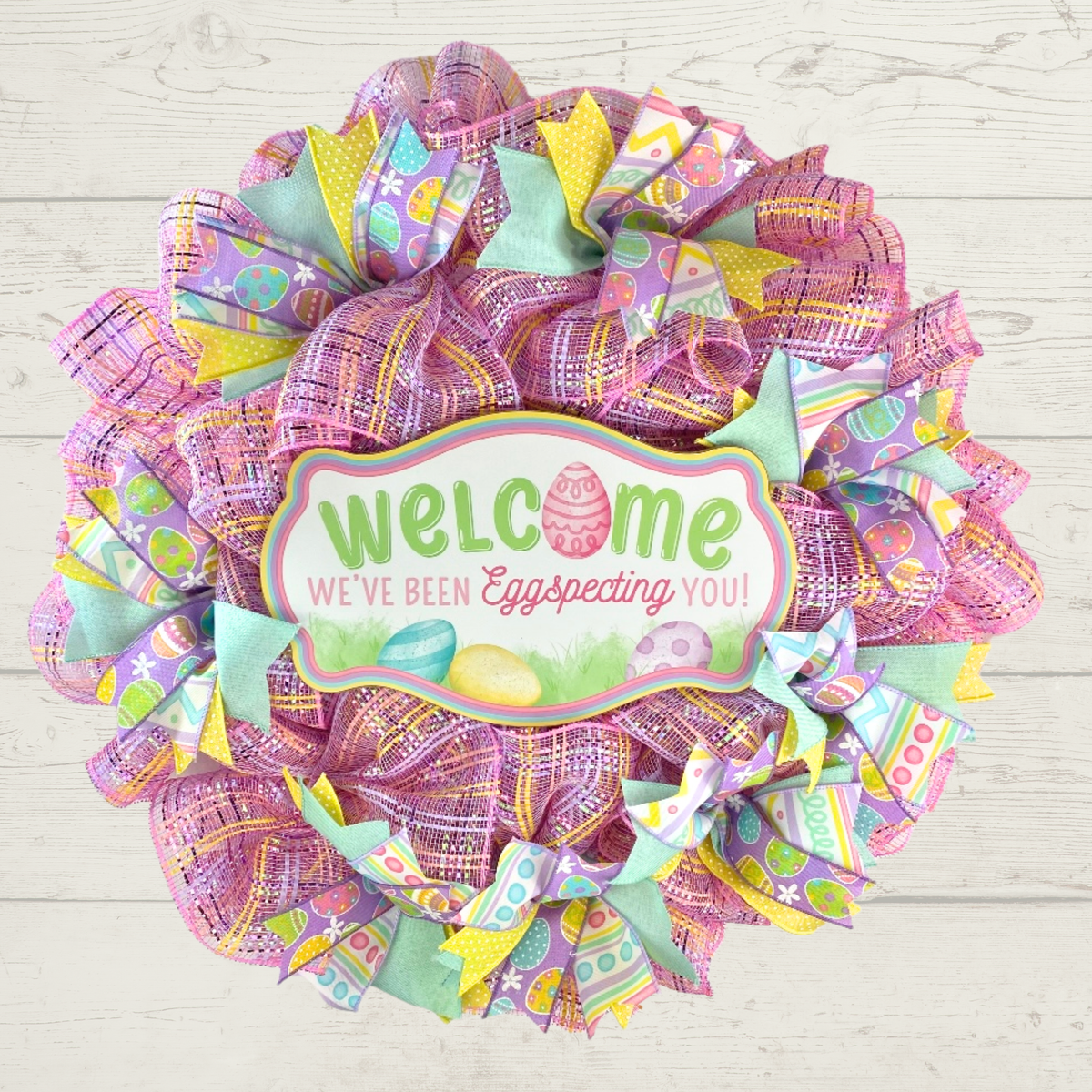 Welcome Easter mesh wreath with pink mesh and pastel ribbons hung on a wall