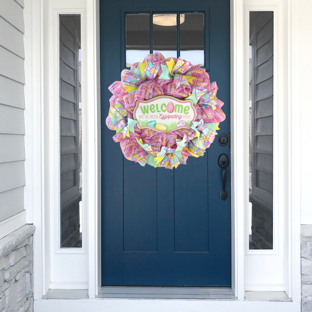 Handmade pastel Easter mesh wreath hanging on a navy blue front door with colorful spring ribbons