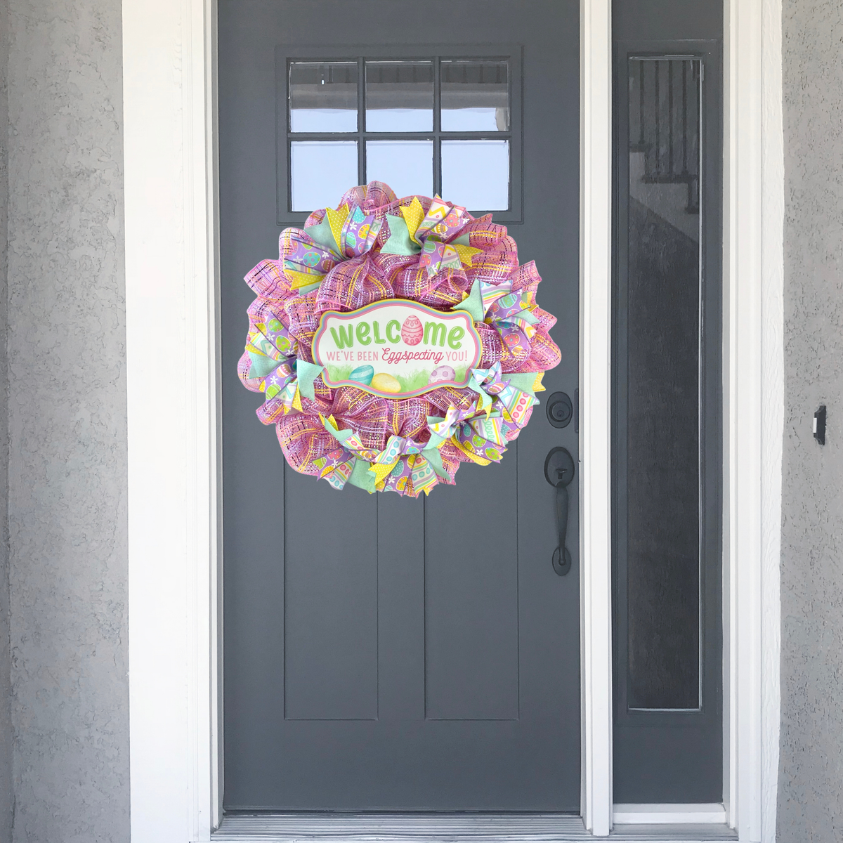 Colorful Easter front door wreath with pink mesh and wooden welcome sign on a gray entry door