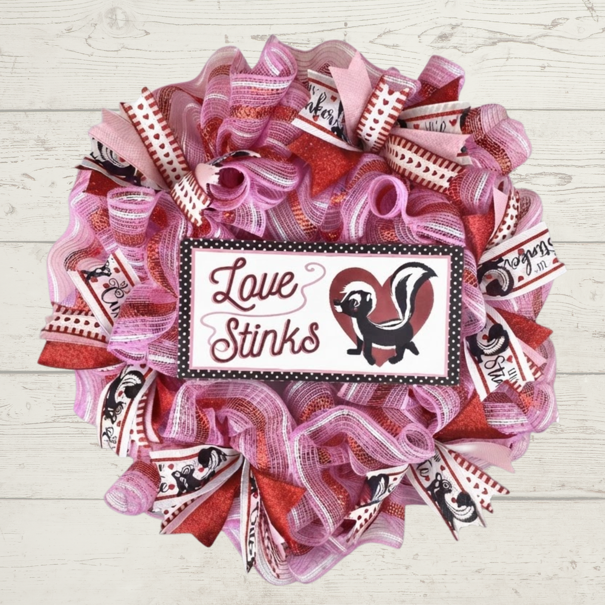 Love Stinks Valentine's Day mesh wreath with pink and red ribbon on shiplap background.