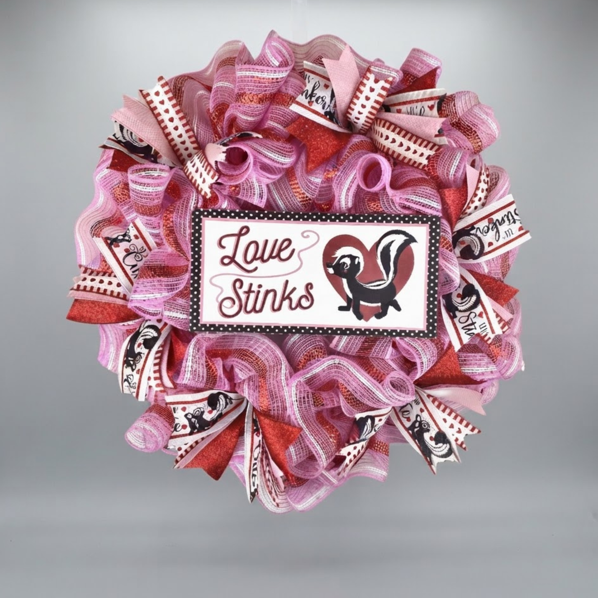 Love Stinks Valentine's Day mesh wreath with pink and red ribbon on gray background.