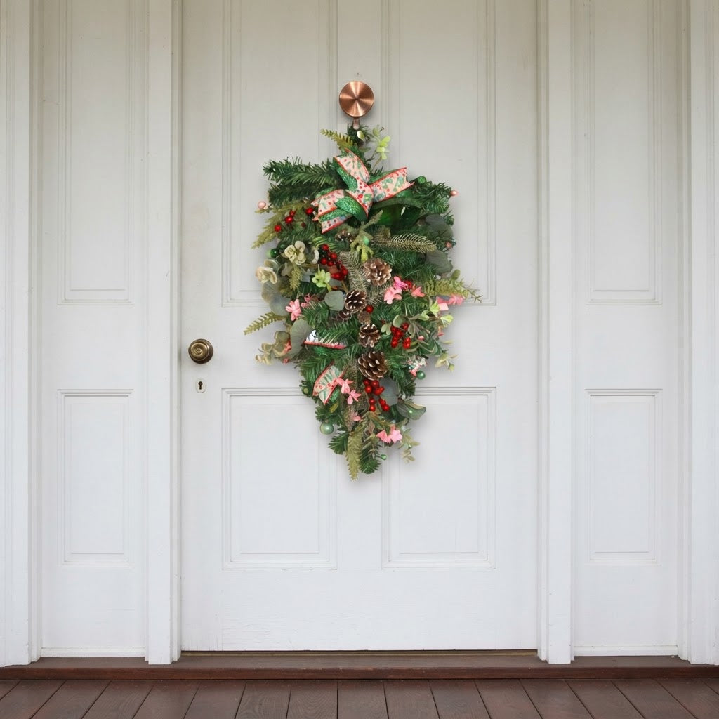 Handmade emerald and pink Christmas teardrop swag displayed on white door